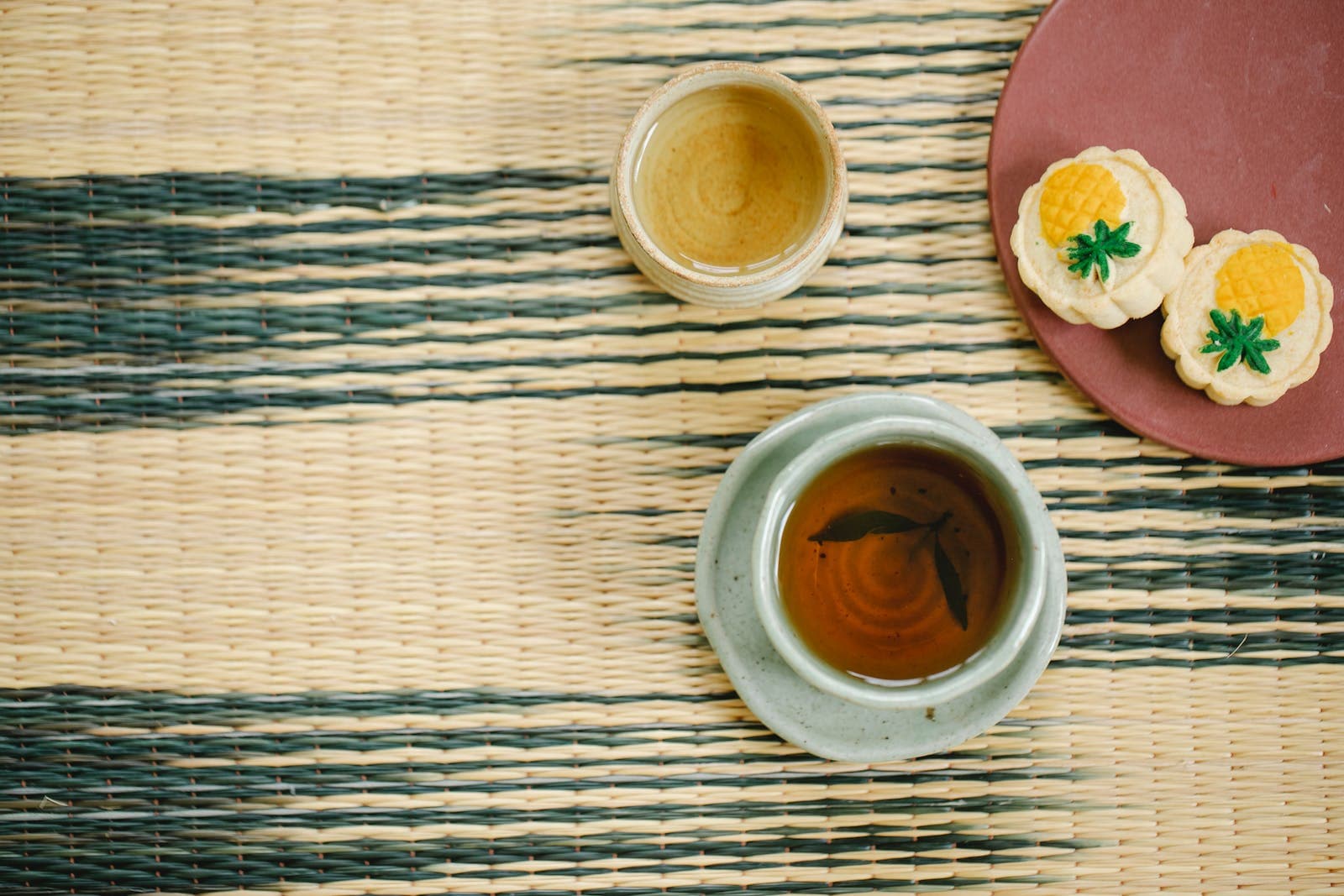 High angle of aromatic black and green tea in ceramic Asian cups near plate with delicious pastries on table
