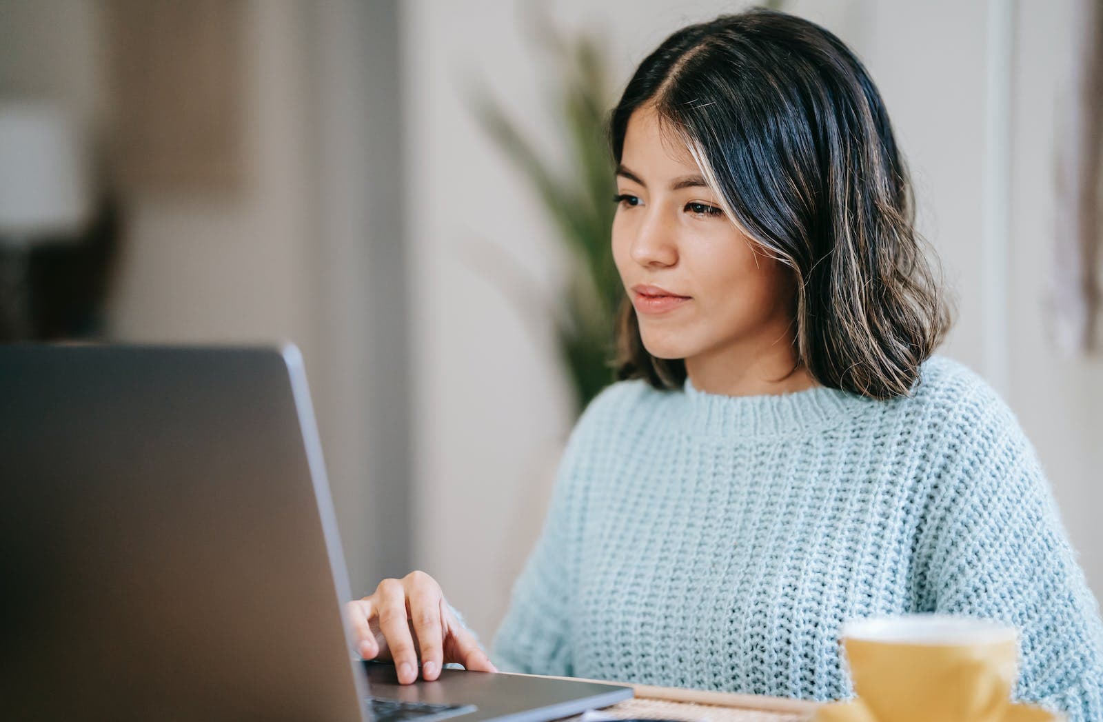 Een vrouw zit met een kopje thee achter de laptop om online enquetes in te vullen
