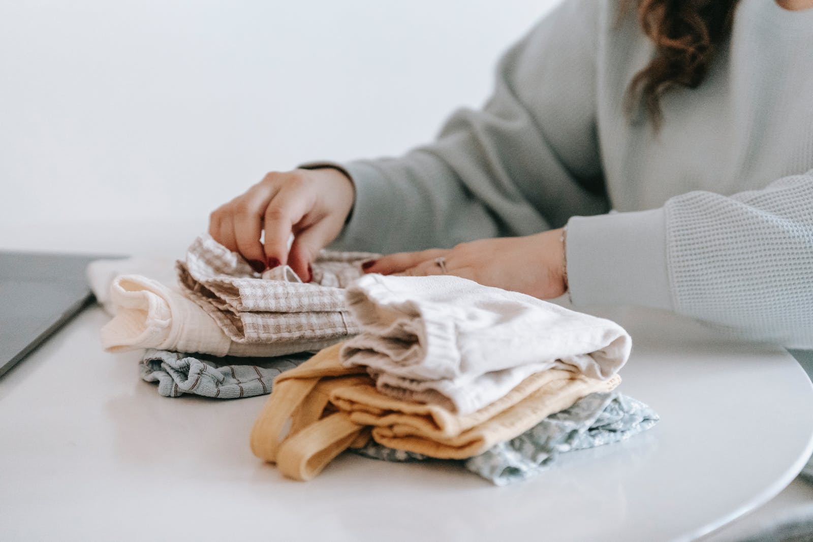 Unrecognizable woman arranging baby clothes at table