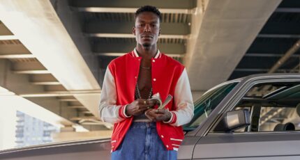 A Man in Red and White Jacket Leaning on the Car while Holding Money