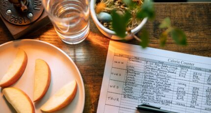 foto van iemand die een papier invult met de ingenomen calorieën, ernaast een plant en gesneden appelpartjes