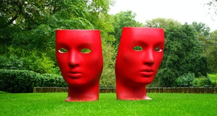 Red Human Face Monument on Green Grass Field