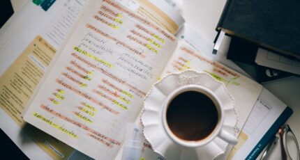 een kop koffie bovenop aantekeningen van iemand die een nieuwe taal leert