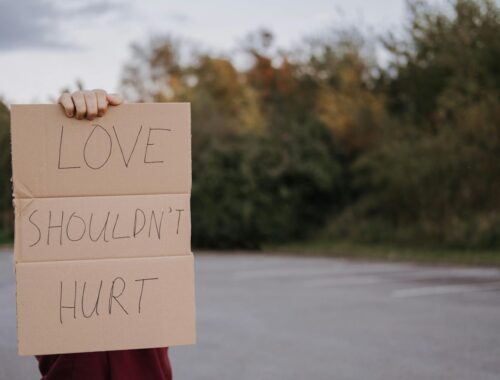 iemand met bindingsangst houdt een bord vast met 'love shouldn't hurt'