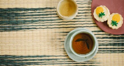 High angle of aromatic black and green tea in ceramic Asian cups near plate with delicious pastries on table