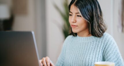 Een vrouw zit met een kopje thee achter de laptop om online enquetes in te vullen