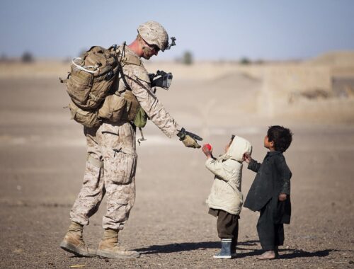 een soldaat geeft rood fruit aan twee kinderen in oorlogsgebied