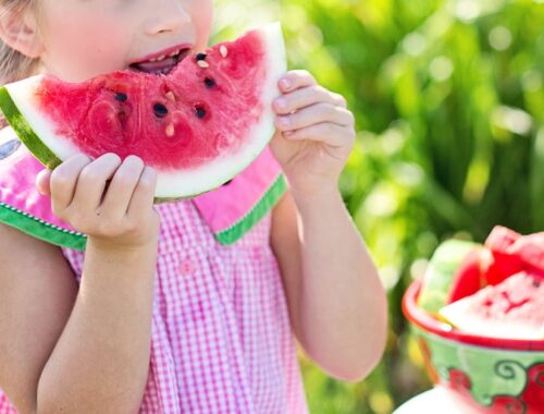 Meisje dat watermeloenfruit naast tafel eet