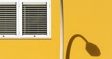 Foto van gele gebouwmuur en raam met witte luiken