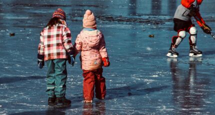 twee kinderen een volwassenen staan met schaatsen op natuurijs