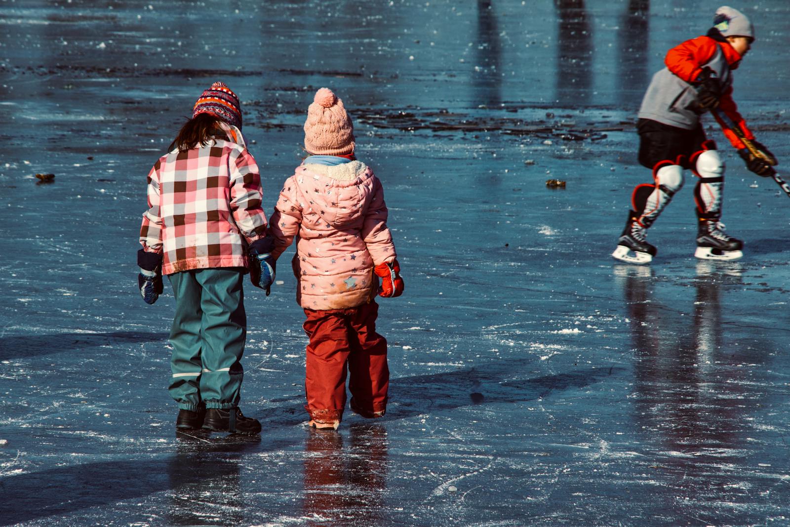 twee kinderen een volwassenen staan met schaatsen op natuurijs