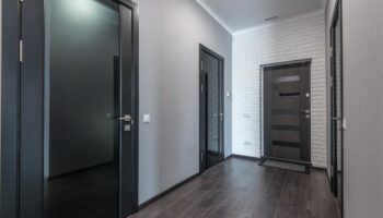 Interieur van lege ruime gang met laminaatvloer en zwarte deuren met glazen delen en wit plafond en grijze geschilderde muren