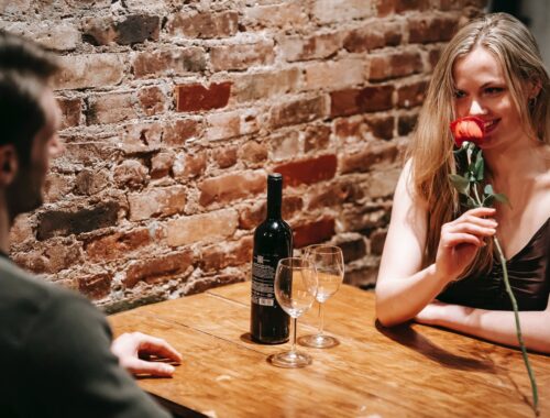 jong koppel zit in restaurant, vrouw houdt rode roos vast en lacht