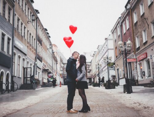 koppel geeft elkaar kus op straat terwijl ze hartjesballonnen vasthouden