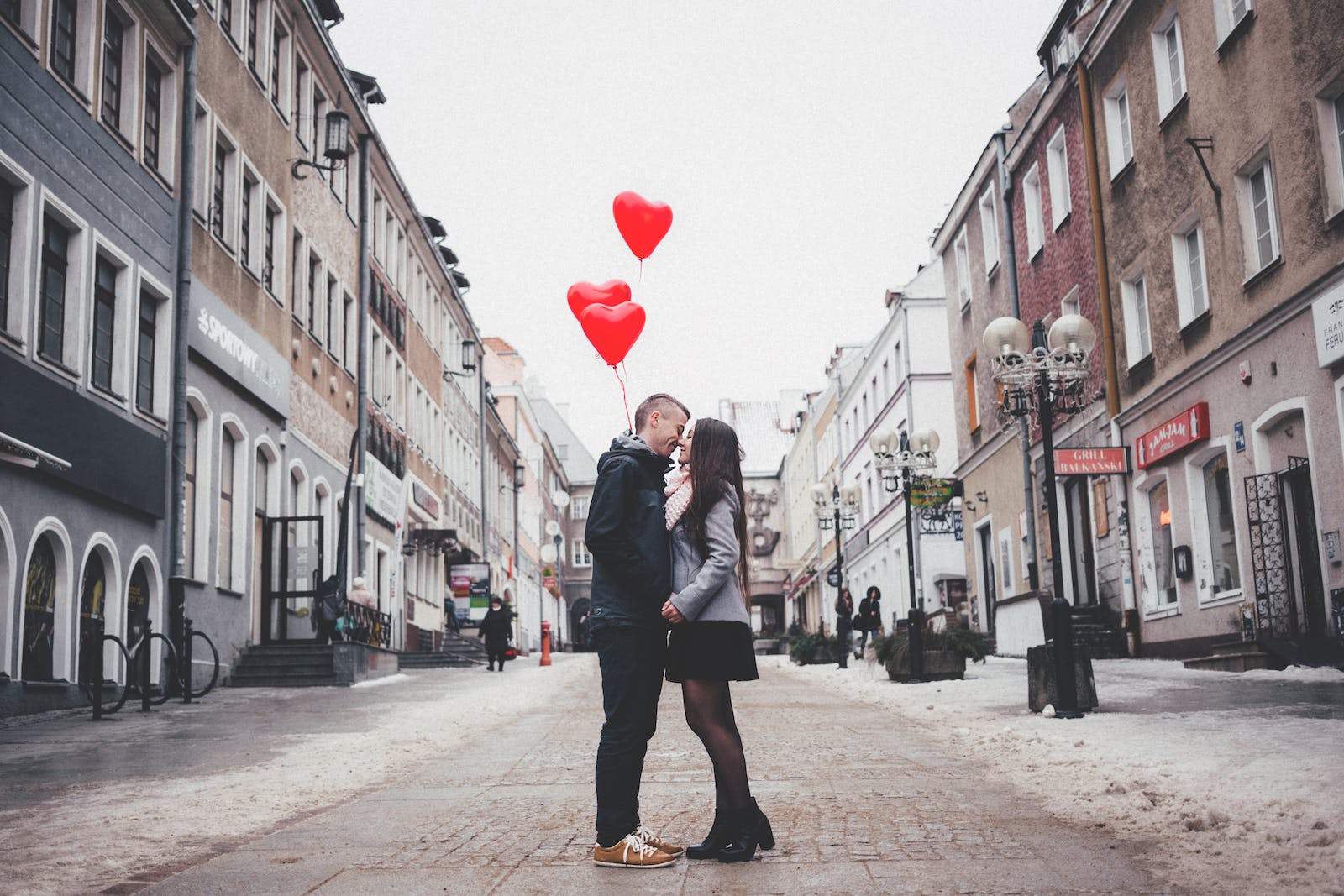 koppel geeft elkaar kus op straat terwijl ze hartjesballonnen vasthouden