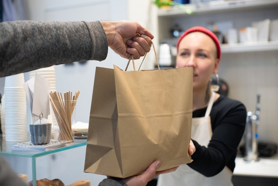 Close-up van restaurantmedewerker die een tas met afhaaleten aan een klant overhandigt