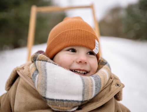 Portret van een blije jongen in de winter, gekleed in een warme jas en een muts, met een sneeuwbedekt landschap op de achtergrond.