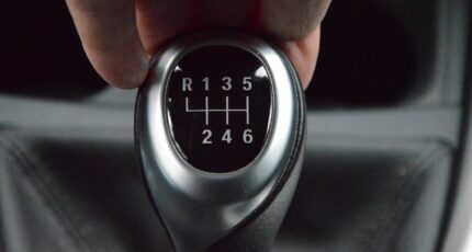 Close-up van een hand die een handgeschakelde versnellingsbak vasthoudt.
