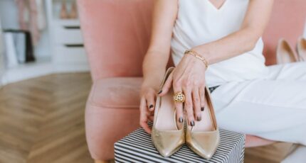 Vrouw in een witte, mouwloze jurk die gouden leren, open tenen hakken draagt.