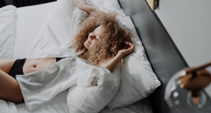 Vrouw in een witte jurk liggend op een bed, met een serene uitdrukking.
