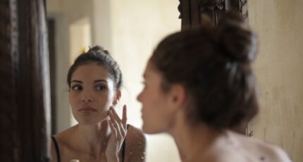 een foto van een vrouw die geen make-up draagt en haar huid controleert in de spiegel