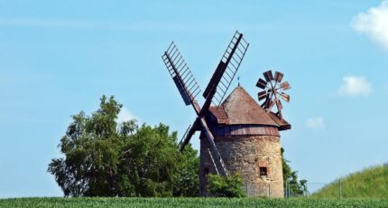 Bruingrijze windmolen naast een groene boom onder een blauwe bewolkte lucht tijdens de dag.