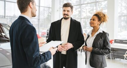 Gelukkig stel bespreekt de aankoop van een auto met een dealer in een showroom. Professionele interactie en advies.