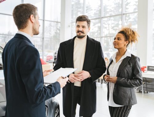 Gelukkig stel bespreekt de aankoop van een auto met een dealer in een showroom. Professionele interactie en advies.