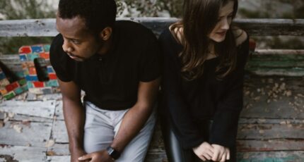 Een stel zit apart op een parkbank, zichtbaar emotioneel, in een buitenomgeving.