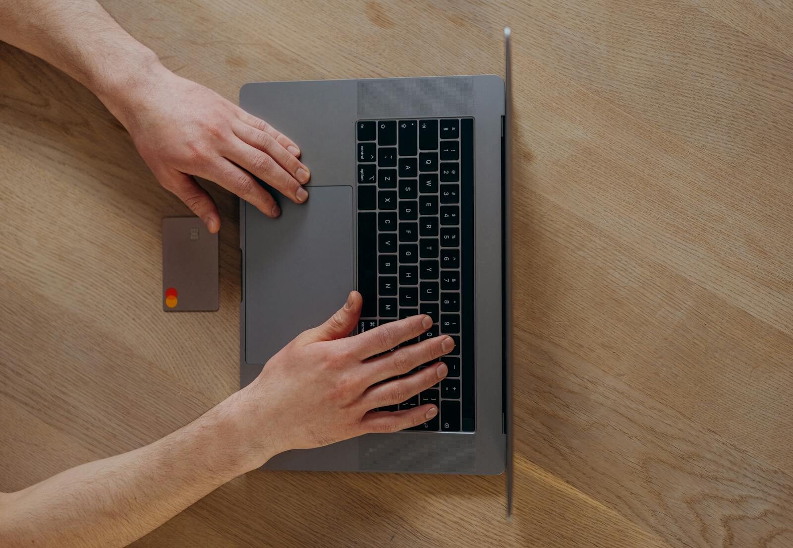 A person using a laptop and credit card for online shopping, viewed from above on a wooden table.